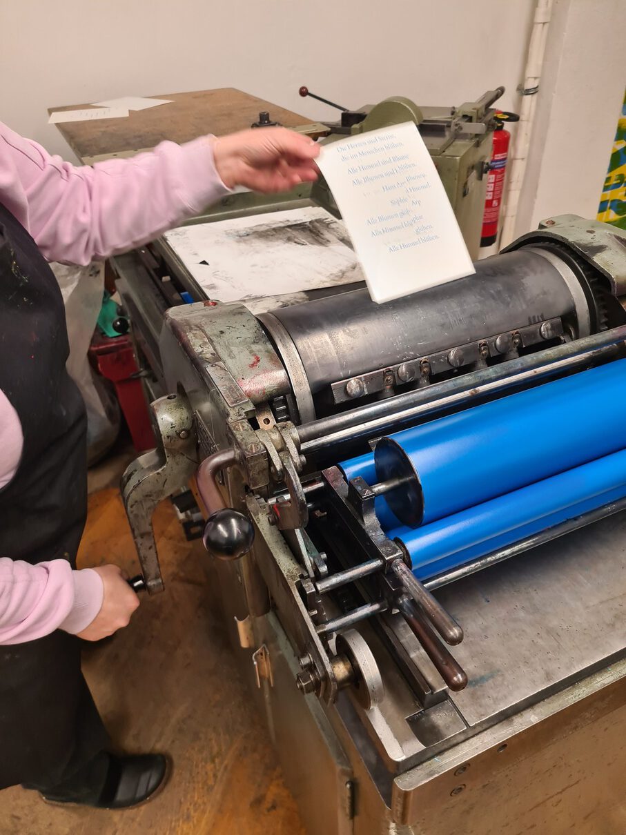 Eine Workshopteilnehmerin entnimmt eine gedruckte Karte von der Korrexandruckpresse.